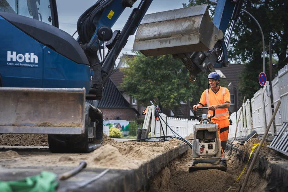 Bagger mit Hoth-Schriftzug, davor ein Arbeiter mit Rüttelplatte